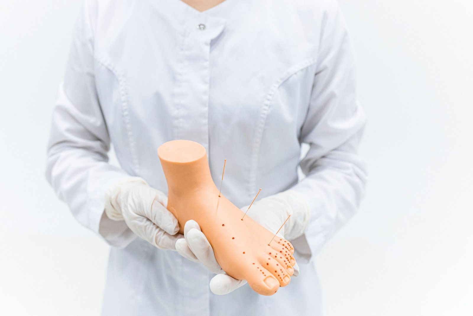 Close-up of medical practitioner holding an acupuncture foot model in a clinical setting.